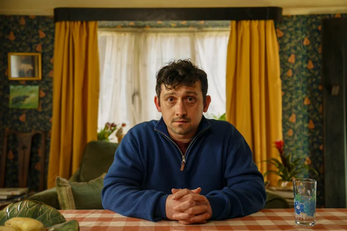 Craig Roberts' character sat in a house, looking wearily at the camera with his hands clasped