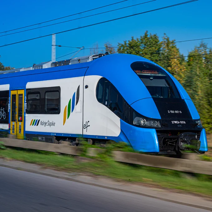 A modern Koleje Mazowieckie train in motion on a sunny day, featuring a vibrant blue color scheme and the company's logo.