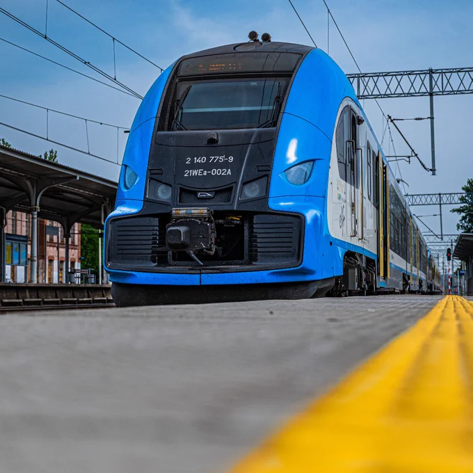 A blue PKP Intercity train at a station, viewed from platform level with a focus on the front car.