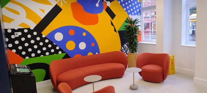 A colourful backdrop on the wall behind orange soft seating at the entrance to the Education Centre.