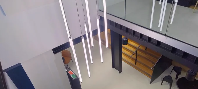 Tube lights coming down from the ceiling onto the floor below on a staircase in the Education Centre building. Stools and other furniture can also be seen.