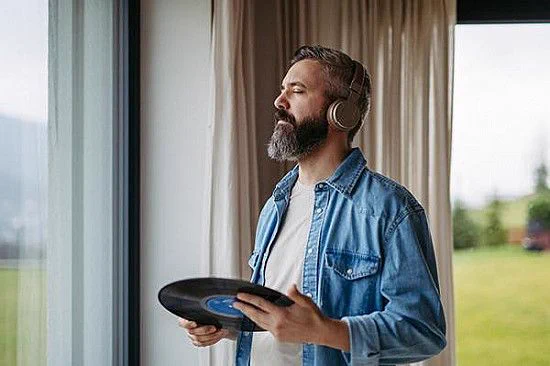 Man listening to music with headphones and holding a vinyl record.