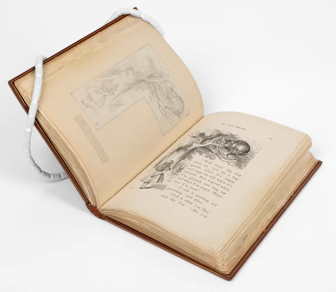 'Alice's Adventures in Wonderland' by Lewis Carroll, opened up to a page showing an illustration of Alice and the Cheshire Cat 