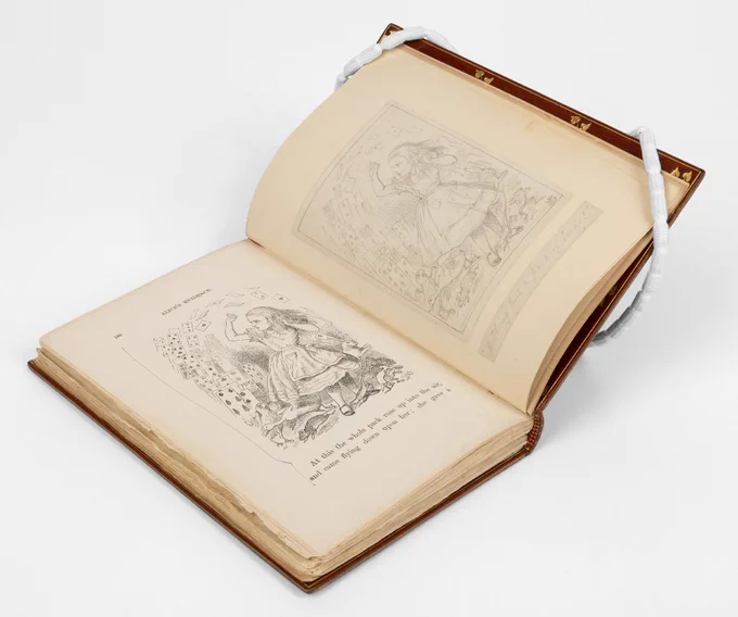 'Alice's Adventures in Wonderland' by Lewis Carroll, opened up to a page showing an illustration of Alice surrounded by playing cards