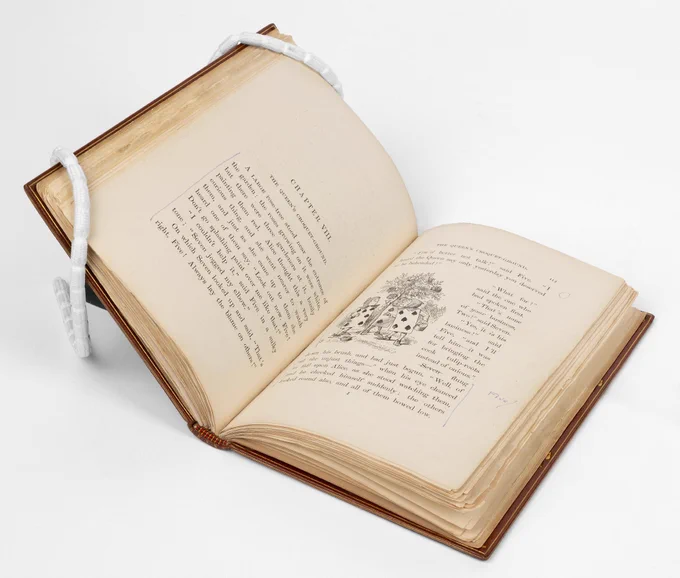 'Alice's Adventures in Wonderland' by Lewis Carroll, opened up to a page showing an illustration of three playing cards under the tree