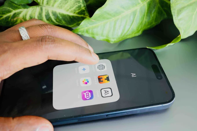 A close up of a person using a cell phone with AI applications on the screen and a green plant in the background.
