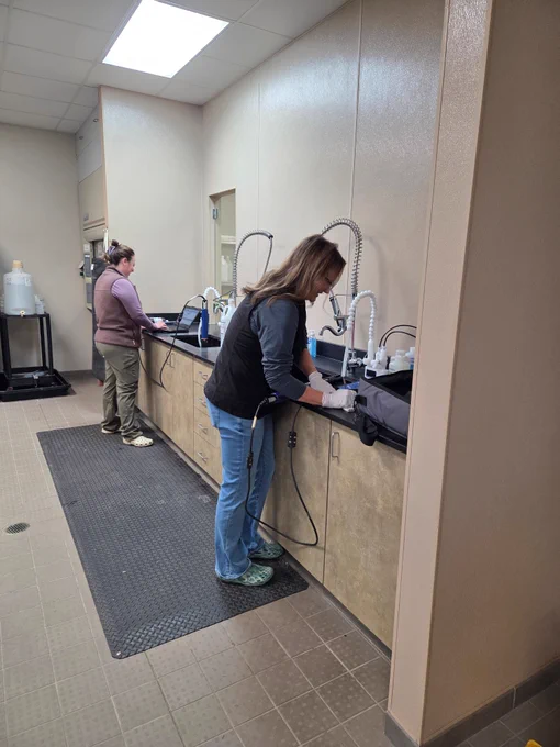 Two hydrologic technicians calibrate equipment in a lab to prepare for field work.
