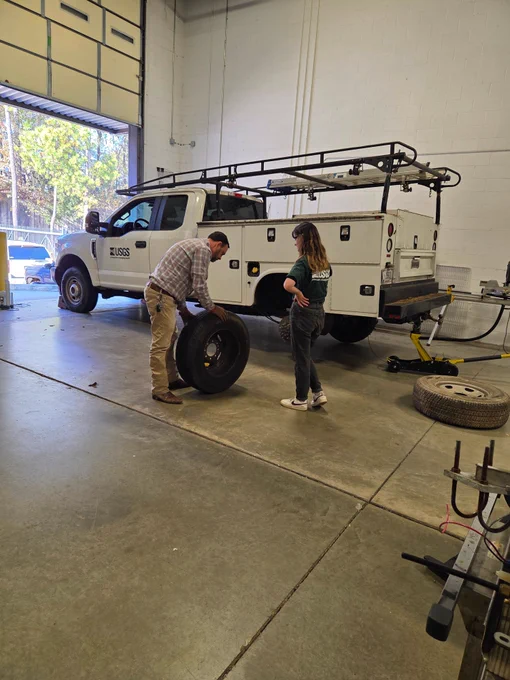 Two technicians look for a nail in a tire from the white truck in the background.