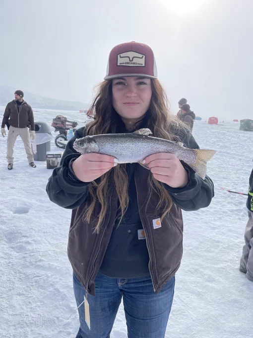 A person standing on a frozen waterbody and holding up a fish. 