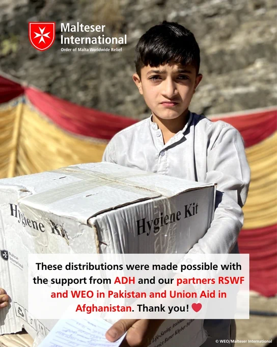 Ein junger Mann hält eine Hygiene-Kit-Verpackung und steht vor roten und gelben Zelten, während die Malteser-Organisation Hilfsprogramme in Pakistan und Afghanistan unterstützt.