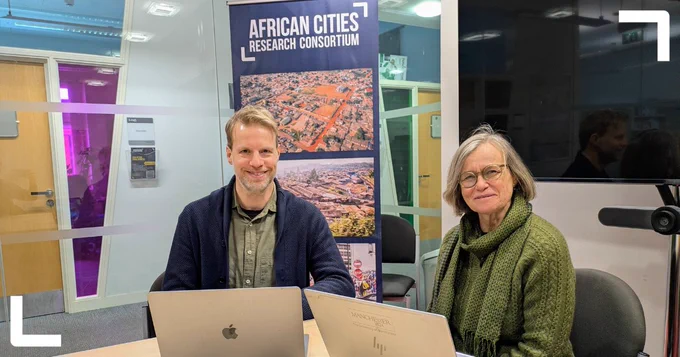 Photo of Tom Goodfellow and Diana Mitlin sitting with their laptops in front of an ACRC branded banner.