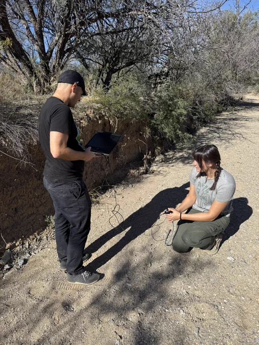 USGS scientists B. Smith and R. Huang collect data from a soil moisture sensor that is located within an incised arid land stream channel with a sandy streambed.