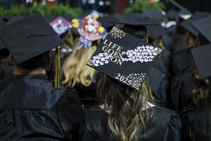 Student sitting in the crowd at Mount Mercy University Commencement wear and embellished mortarboard with the saying, "Life Goes On"