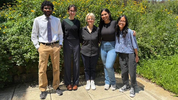 Group photo of five students standing side by side outdoors.