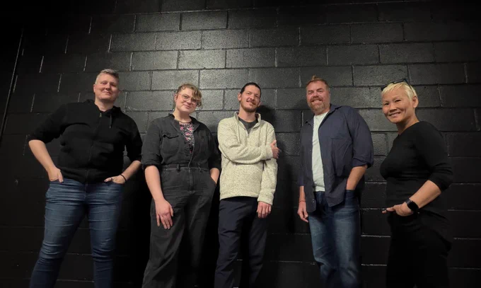 A group picture of Jules Dameron, NYDT Artistic Director, Nikolya Sereda, Assistant Artistic Director, and Meat Expectations writers Seth Gore, JW Guido, and MoMo Holt. All stand in front of a black brick wall and in various poses smiling.