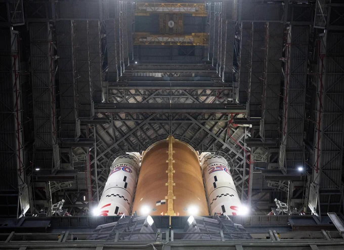 NASA’s Space Launch System rocket is seen inside high bay 3 of the Vehicle Assembly Building as Artemis II crewmembers board their Orion spacecraft atop the rocket during the Artemis II countdown demonstration test, Saturday, Dec. 20, 2025, NASA’s Kennedy Space Center in Florida. The perspective of the image is from below the rocket looking up. The core stage is orange and the boosters on either side are white. Platforms can be seen on either side of the rocket. Credit: NASA/Joel Kowsky