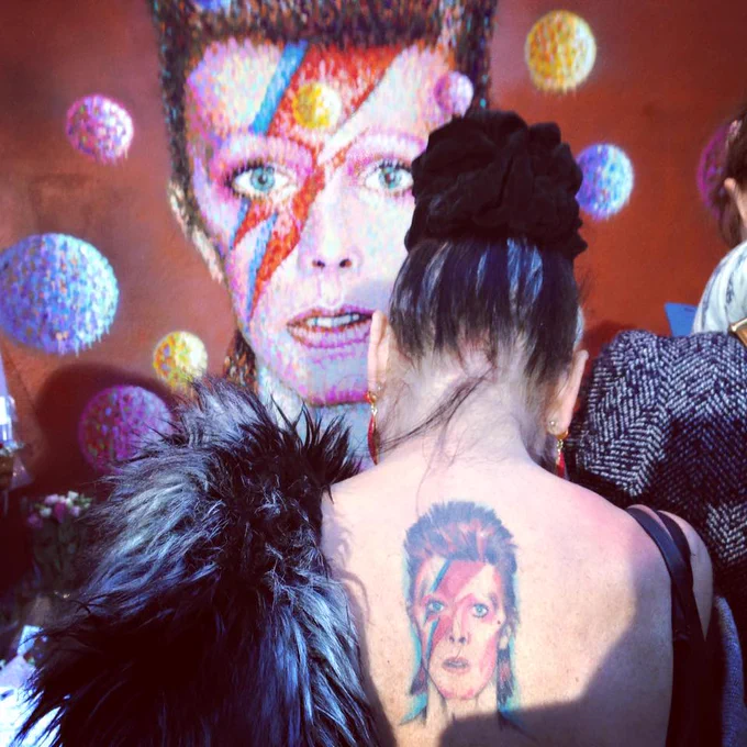 A woman with a Ziggy Stardust David Bowie tattoo on her back stands in front of the David Bowie mural in Brixton on the day he died in 2016