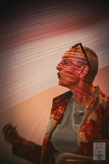 A person is shown talking with streaks of lighting projected onto the wall and her face.