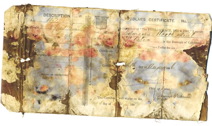 A damaged and stained 19th-century paper certificate with faded handwriting. It is a pedlar’s licence issued to James Lidman of North Street, Colchester, on 4 August 1886, giving his age as 43 and his height as 5 foot 6 inches. The document is browned and worn with large patches of blue and pink water damage, holes, and torn edges.