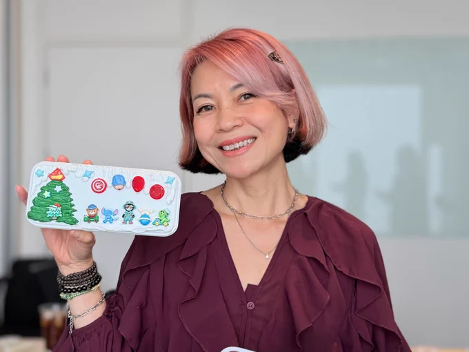 An Oracle employee holds a decorated white pencil case, featuring a Christmas tree and cartoon characters.