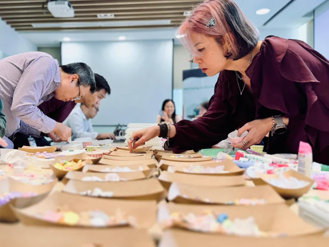 A group of Oracle employees are gathered around a long table, participating in a craft activity. 