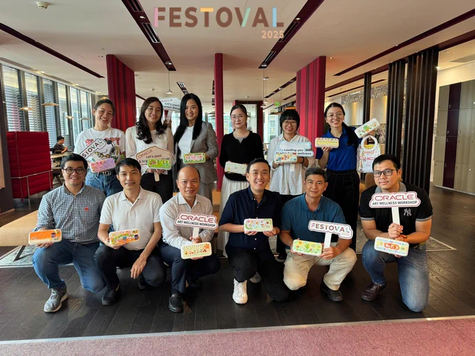 A group of Oracle employees are in two rows, holding their craft and signs that say "FESTOVAL 2025", "ORACLE ART WELLNESS WORKSHOP"