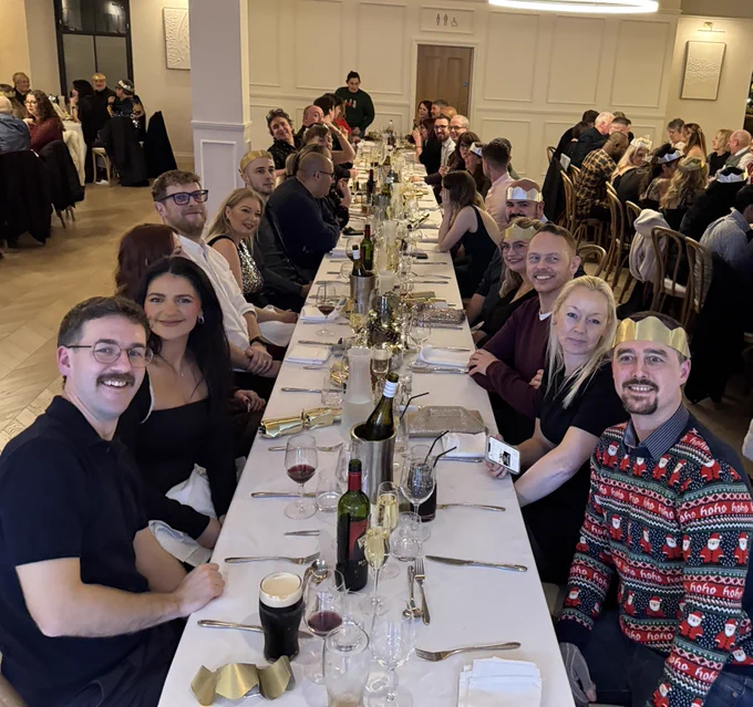 Photo of  BCCIT staff members and their partners enjoying the annual Christmas party, which this year was held at Ty Glyn in Ciliau Aeron, near Lampeter in Ceredigion, Wales. Guests are seated at long tables with festive drinks, capturing the relaxed, sociable atmosphere described in the December 2025 Insight blog.