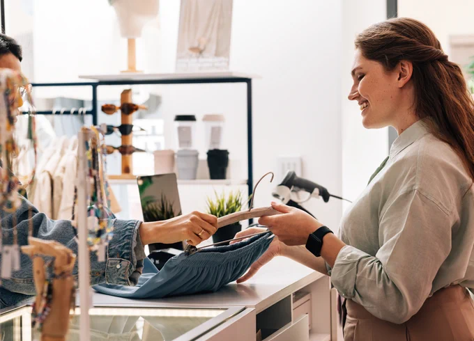 Customer handing a folded shirt to a retail worker at a modern clothing store counter.