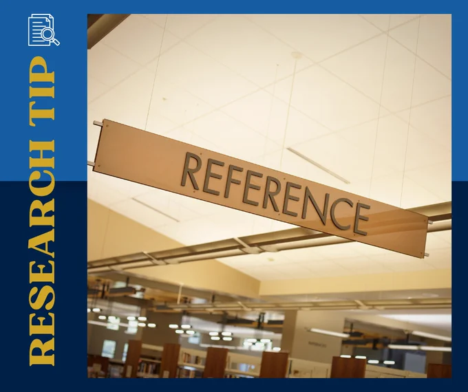 A brown sign hanging from a tan library ceiling that says Reference.