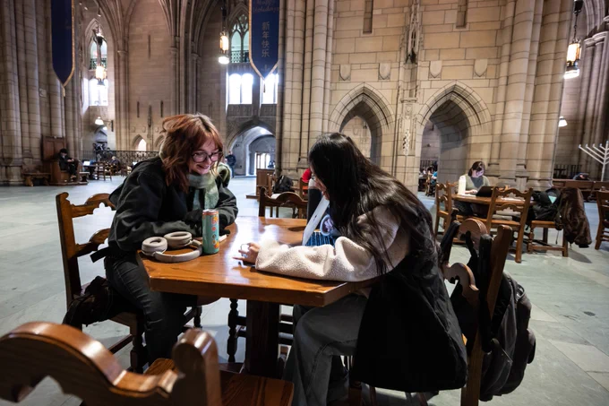 Two people engaged in conversation while sitting at a table inside the grand, vaulted interior of the Cathedral of Learning.