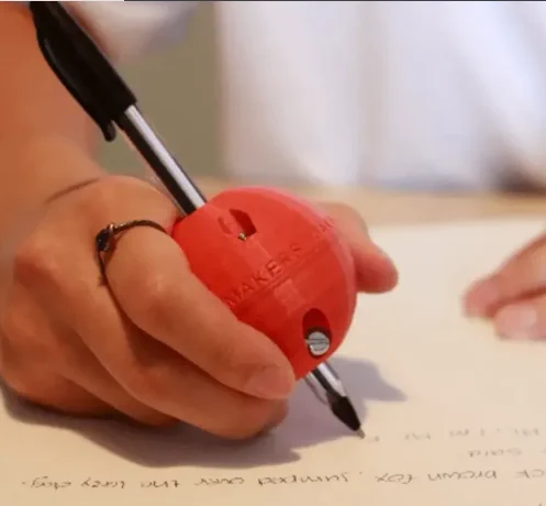  A person is writing on paper utilizing an assistive device  a 3
d printed red ball to hold the pen.