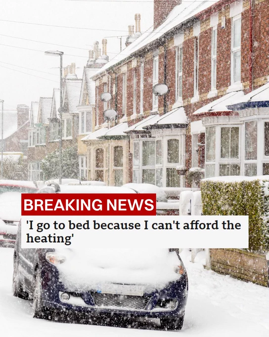 A snow-covered street with lined residential houses during a snowfall, with a car in the foreground partially covered in snow. The text overlay reads "BREAKING NEWS 'I go to bed because I can't afford the heating'".