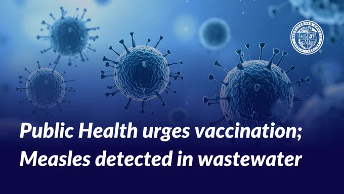 Image featuring an illustration of measles viruses with a backdrop of a blue gradient. Text reads 'Public Health urges vaccination; Measles detected in wastewater.'