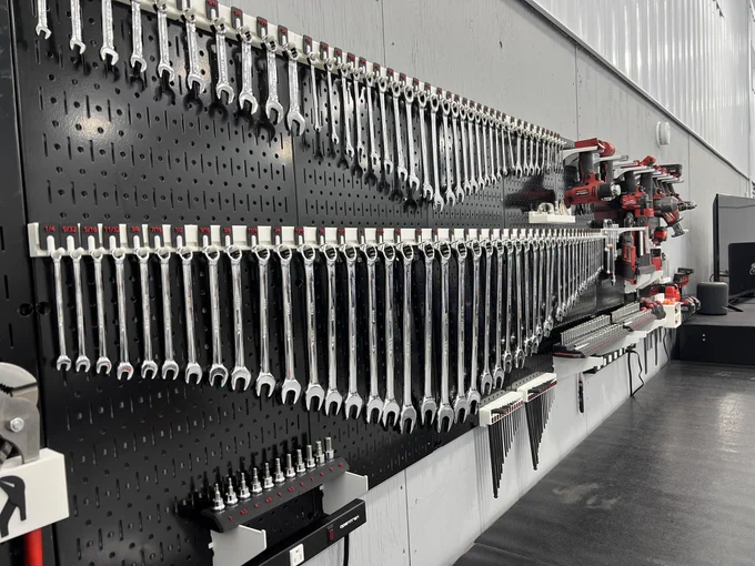 A wall-mounted black Wall Control metal pegboard filled with neatly organized chrome combination wrenches in multiple sizes, arranged in straight rows. Power tools and socket sets are mounted on the right side, creating a clean, professional workshop display.