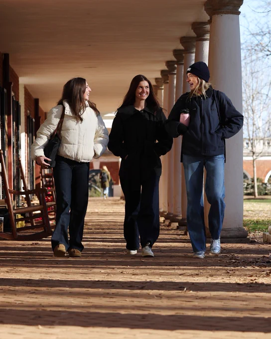 Three UVA students walk down a brick walkway in warm apparel.