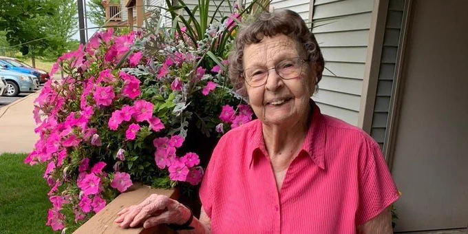 Photo of older woman on her porch next to pink flowers