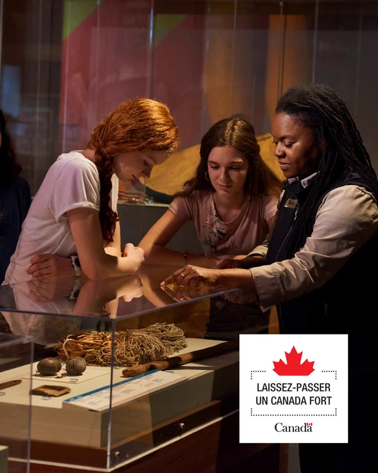 Dans une exposition muséale, un guide présente des histoires en lien à des objets à deux jeunes visiteurs captivés. Avec le logo du Laissez-Passer un Canada Fort.