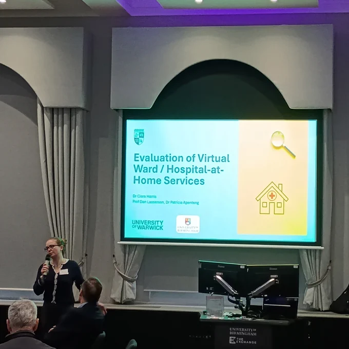 Dr Ciara Harris talking in front of a presentation entitled 'Evaluation of Virtual Ward / Hospital-at-Home Services'