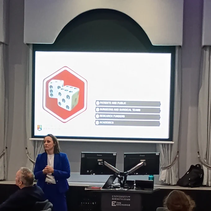 Prof Amy Grove talking in front of a slide showing the groups impacted by trial results not being implemented - patients and the public, surgeons & surgical teams, research funders, and academics.