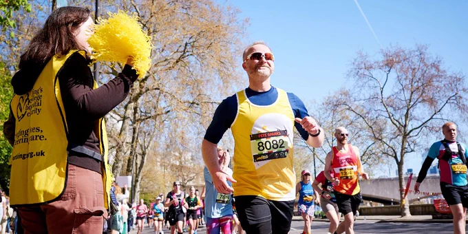 Runner wearing a yellow vest participating in the London Landmarks Half Marathon on a sunny day with leafless trees in the background.