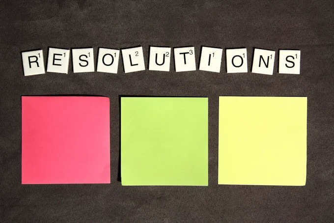 Scrabble tiles spelling 'Resolutions' above colorful sticky notes for goal setting.