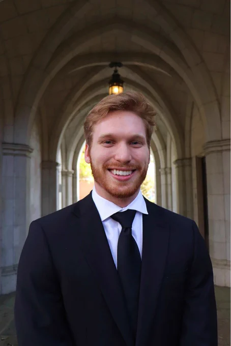 Michael Lafferty wearing a black suit and tie and standing in front of an arched walkway with a lantern.