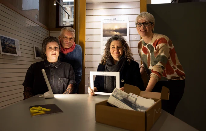 A group of four people sit at a table with the contents of a Wintering Well Box designed to support anyone experiencing low mood or SAD.