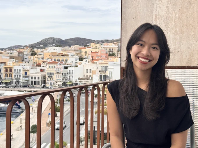 Michelle smiling, sitting on a balcony looking over a European city and waterfront.