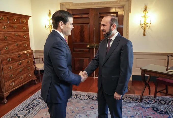 Secretary Rubio shakes hands with Armenian Foreign Minister Mirzoyan in Washington, DC on January 13, 2026. They stand on a rug in a room with wooden double doors with wall sconces each side, a tall wooden bureau and a chair behind the Secretary, and a wooden desk and chair behind the Foreign Minister. (State Department/Freddie Everett)
