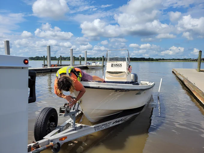 Someone leaning over the front of a boat attaching the boat to a trailer.