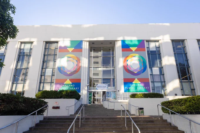 Exterior view of Oakland Public Library with colorful banners on either side of the entrance and stairs leading up to the building.