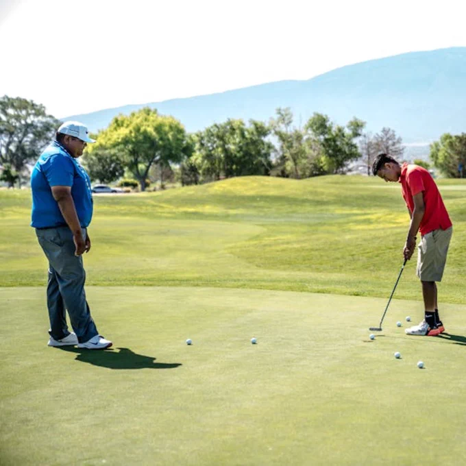 Two men practicing putting on a sunny golf course with mountain views.