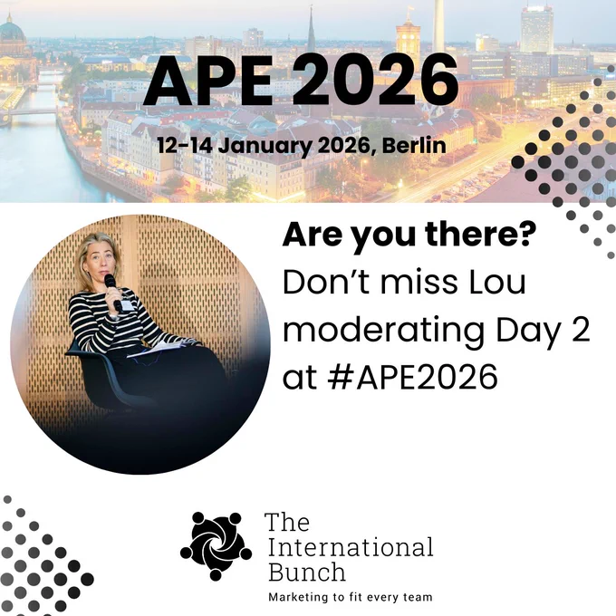 Promotional graphic for APE 2026, taking place 12–14 January 2026 in Berlin, with a city skyline background. Text reads: 'Are you there? Don’t miss Lou moderating Day 2 at #APE2026.' Below is The International Bunch logo and tagline. A circular photo shows Lou sitting on a chair, holding a microphone, wearing a striped top