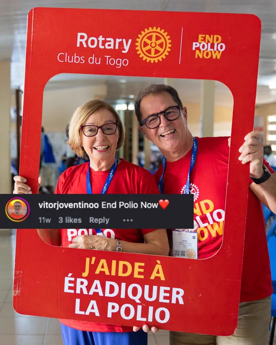 Two individuals are smiling while holding up a large red frame that features the Rotary International logo and the text "End Polio Now." They are wearing matching red t-shirts in an indoor setting.